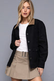 Woman wearing a black jacket over a white shirt and beige skirt on a gray background