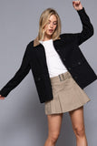 Woman wearing a black jacket, white shirt, and beige skirt on a gray background