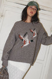 Woman wearing a gray sweater with a fox design against a white wall.