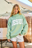 Woman wearing a light green sweatshirt with 'JESUS' printed on it, standing outdoors.