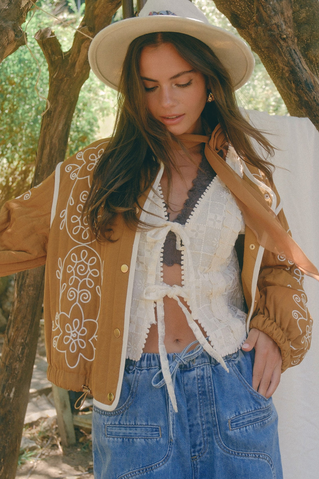 Woman wearing a tan embroidered jacket, white top, and blue jeans outdoors.