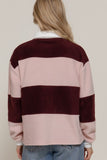 Person wearing a striped sweater with maroon and pink colors on a plain background