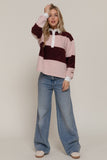 Person wearing a pink and burgundy striped sweater with blue jeans on a plain background