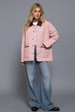 Woman wearing a pink quilted jacket and blue jeans on a gray background