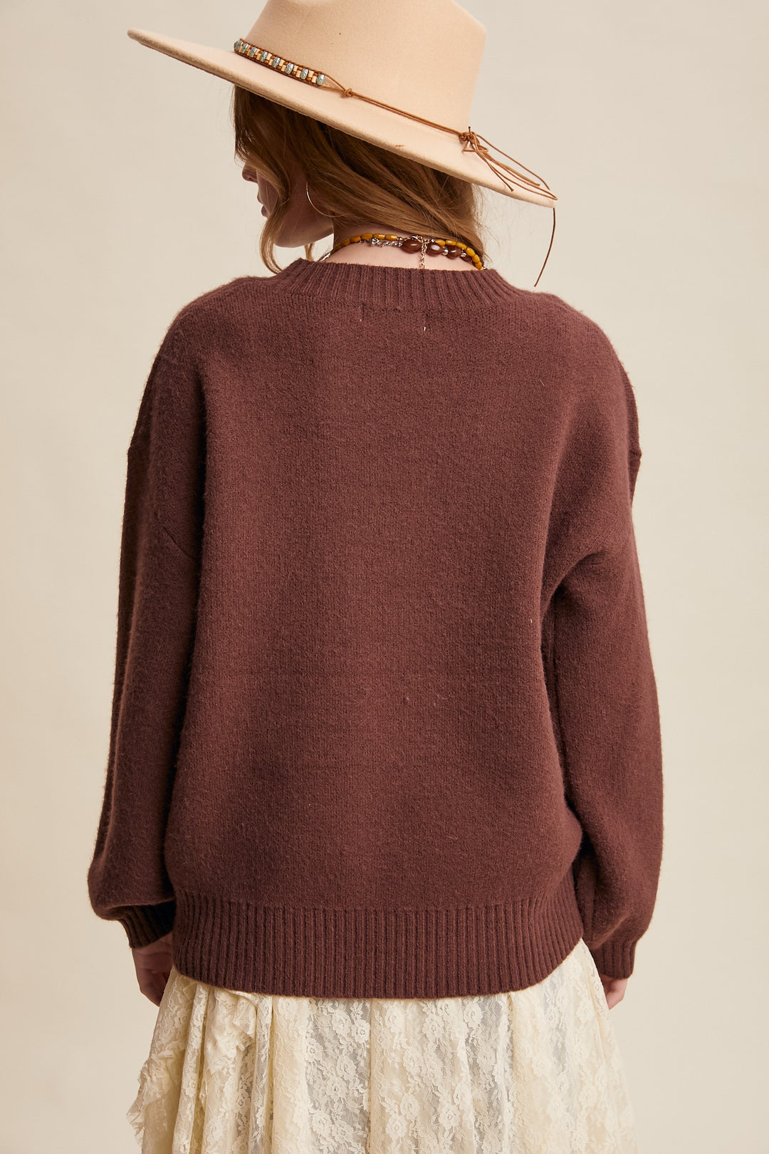 Person wearing a brown sweater and beige hat on a beige background