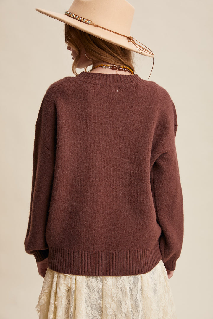 Person wearing a brown sweater and beige hat on a beige background