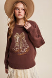 Woman wearing a brown sweater with a gold design and a beige hat on a beige background