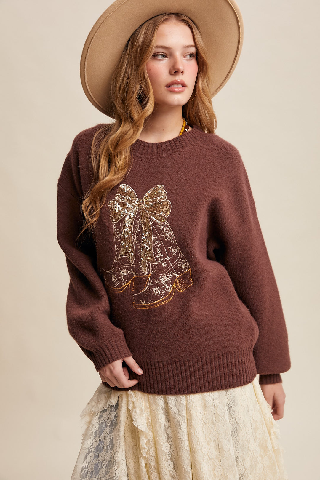 Woman wearing a brown sweater with lace details and a beige hat against a beige background