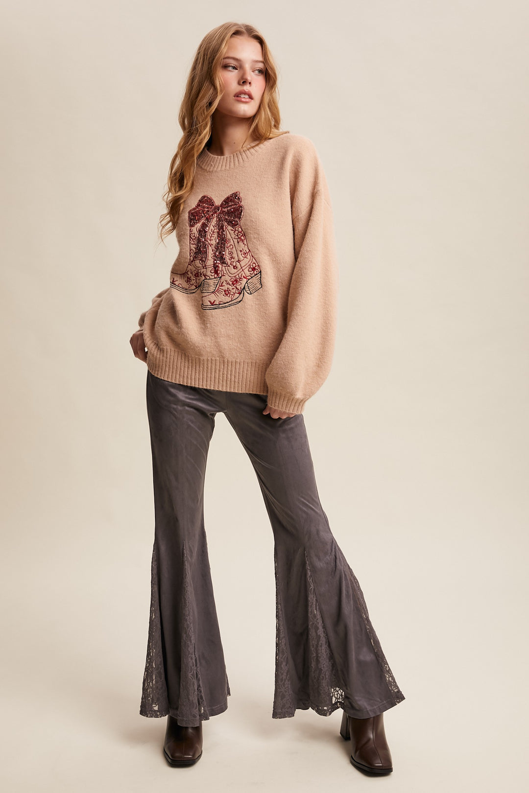 Woman wearing a beige sweater with a floral design and flared pants on a beige background