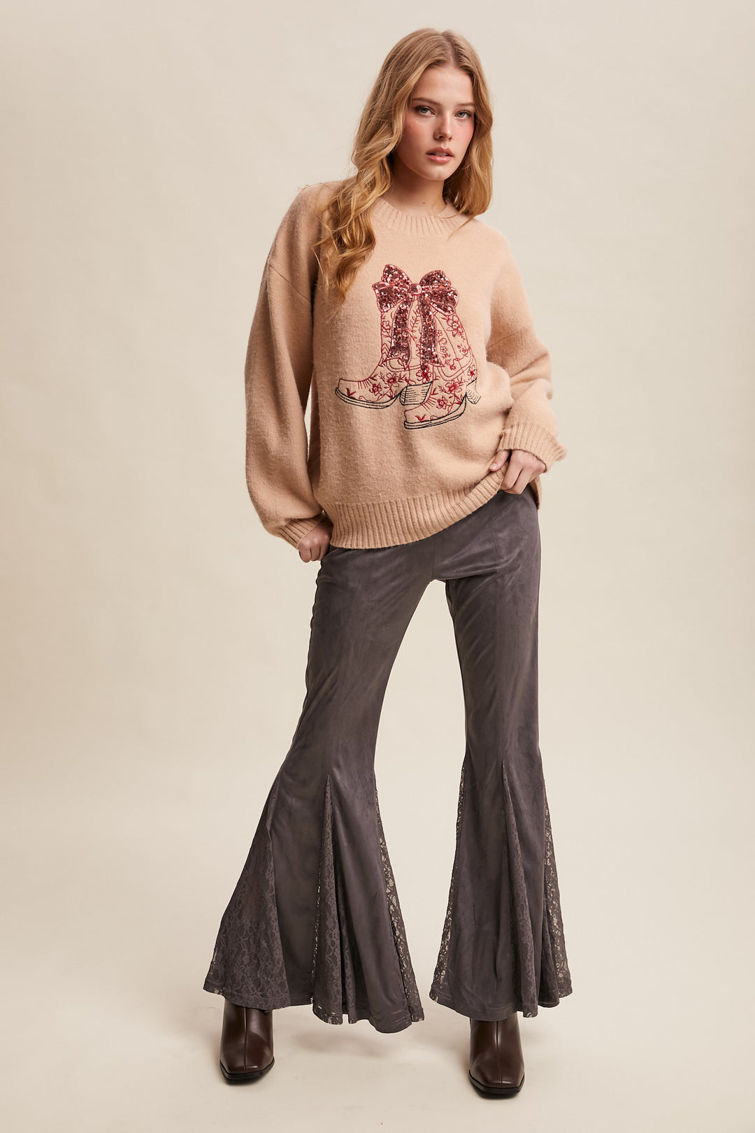 Woman wearing a beige sweater with a floral design and flared pants on a beige background