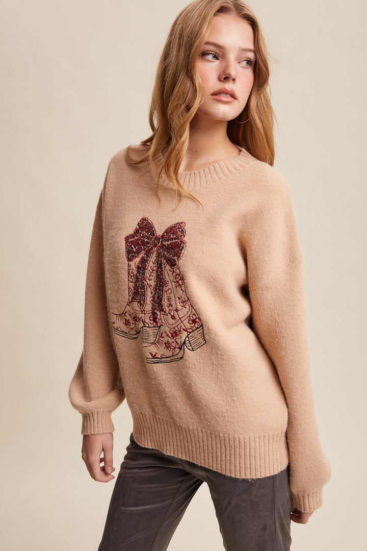 Woman wearing a beige sweater with a decorative bow design on a plain background