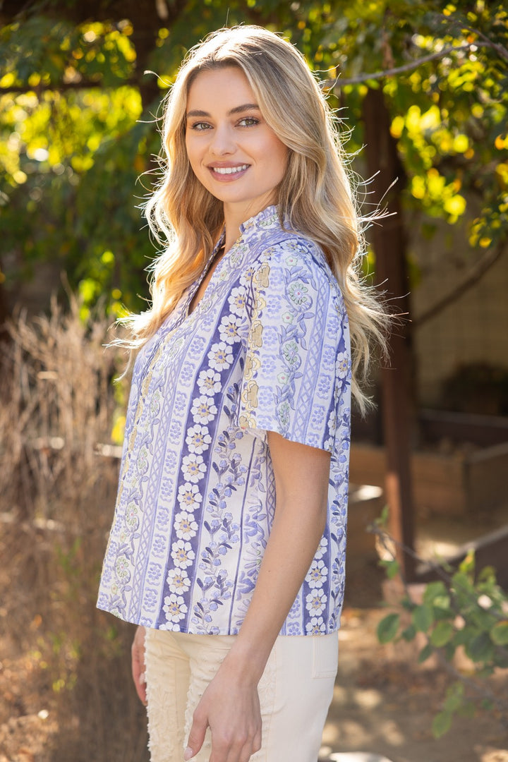 Woman wearing a blue floral blouse standing outdoors with greenery in the background
