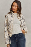 Woman wearing a floral jacket over a white sweater and blue jeans on a gray background