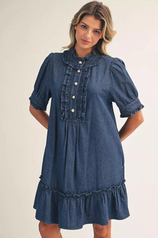 Woman wearing a blue denim dress with ruffled details on a plain background