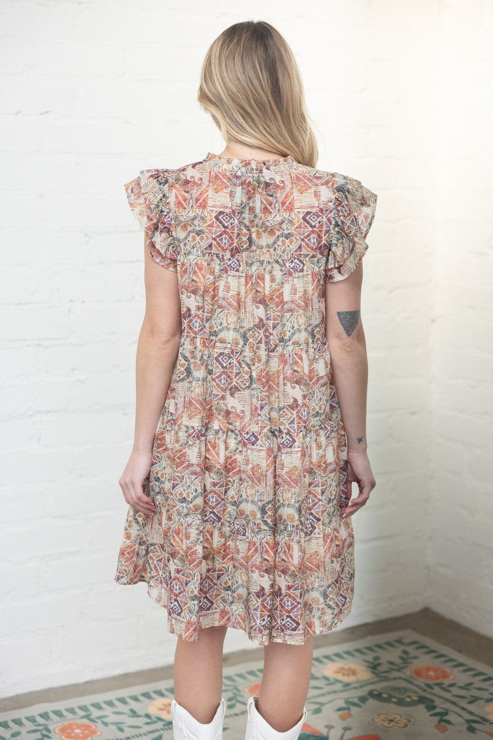 Woman wearing a floral dress against a white brick wall.
