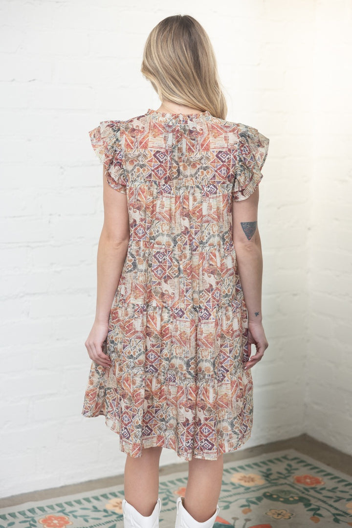 Woman wearing a floral dress against a white brick wall.