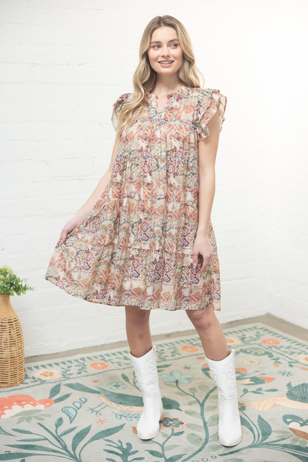 Woman wearing a floral dress standing on a patterned rug with a white wall background