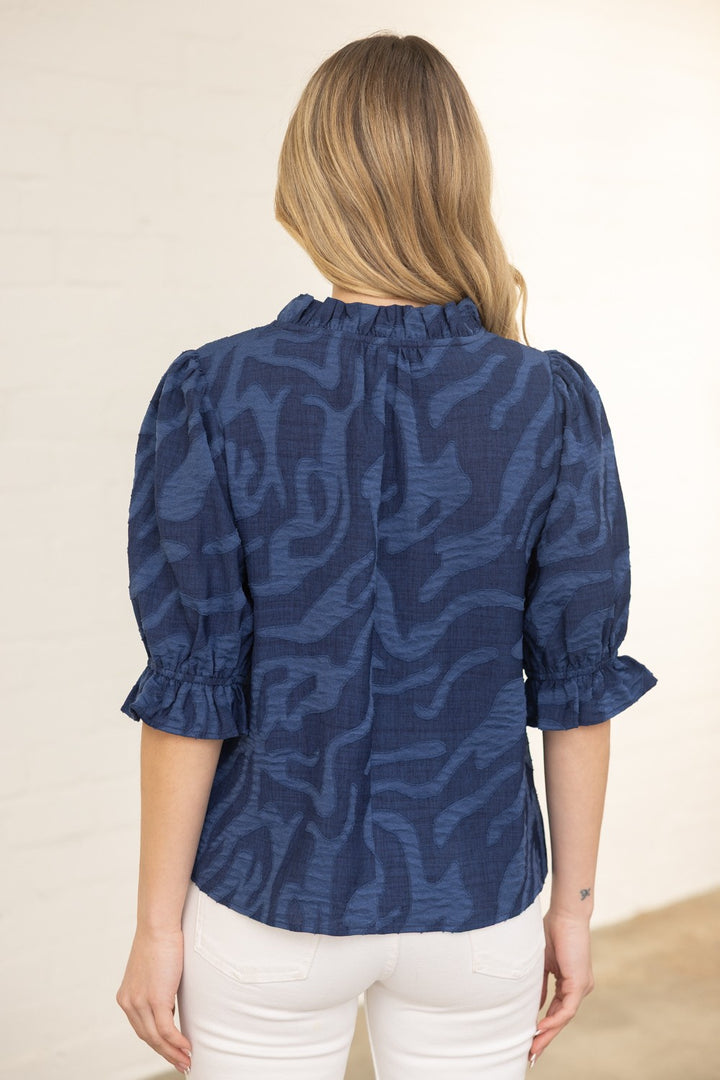 Woman wearing a blue patterned blouse with white pants on a beige background