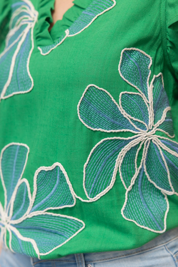 Green blouse with floral embroidery on a person wearing jeans.