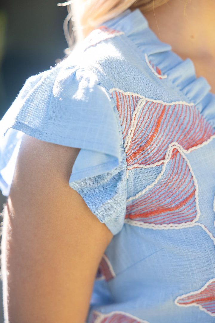 Light blue blouse with red floral embroidery on a blurred background
