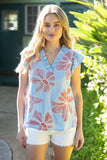 Woman wearing a light blue sleeveless top with pink floral patterns outdoors.