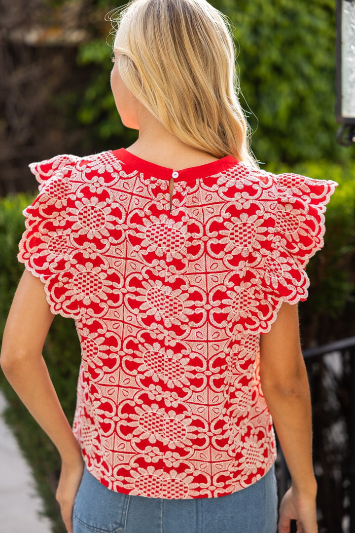 Woman wearing a red and white lace top with a blurred green outdoor background