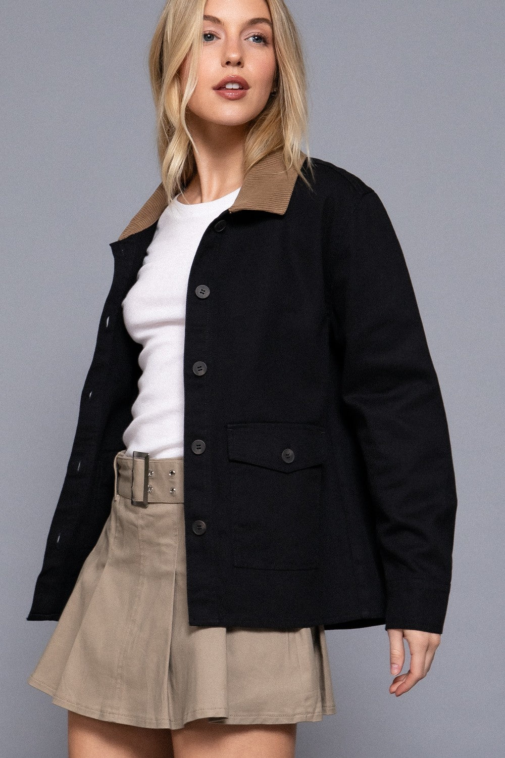 Woman wearing a black jacket with a brown collar and beige skirt on a gray background