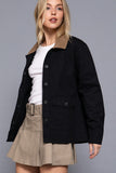 Woman wearing a black jacket with a brown collar and beige skirt on a gray background