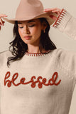 Woman wearing a beige sweater with 'blessed' text and a matching hat against a neutral background