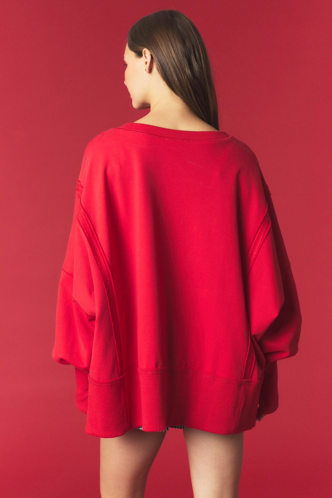 A woman shown from the back wearing an oversized bright red sweatshirt against a solid red studio background.