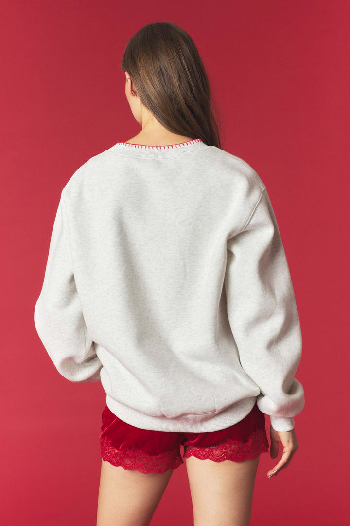 A woman shown from behind wearing a light gray heather crewneck sweatshirt and red lace-trimmed shorts against a solid red background.