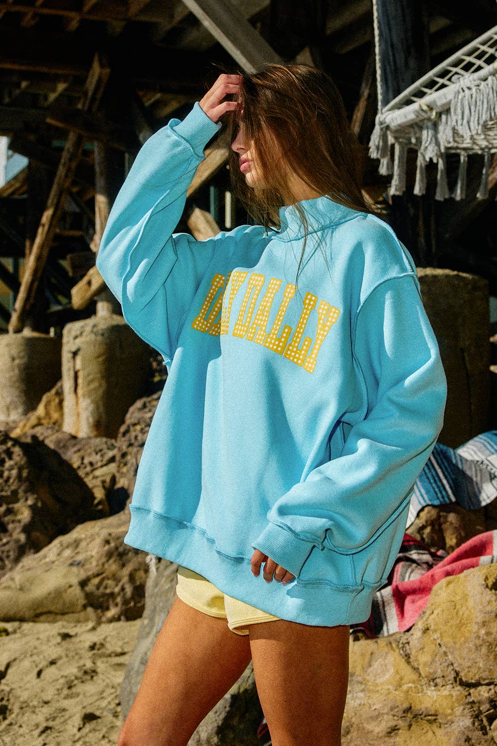 Person wearing a light blue sweatshirt with yellow text on a beach.
