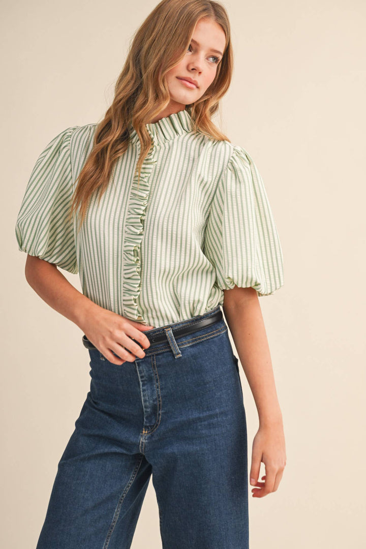 Woman wearing a green and white striped blouse with ruffled details and blue jeans on a beige background