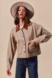Woman wearing a beige jacket with brown collar, blue jeans, and a beige hat on a beige background