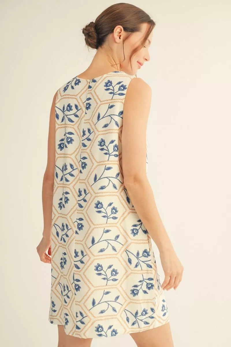 Woman wearing a sleeveless dress with blue floral pattern on a beige background