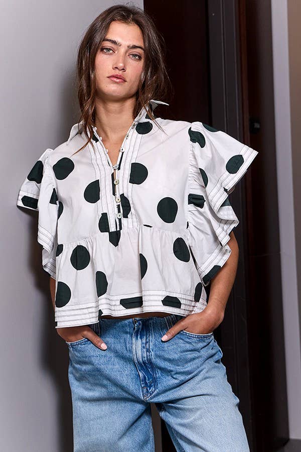 Woman wearing a white top with black polka dots and blue jeans against a neutral background
