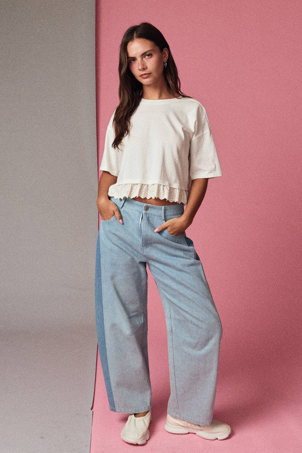 Woman wearing a white top and light blue jeans against a pink background