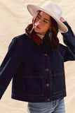 Woman wearing a navy jacket with a red collar and white hat on a beige background
