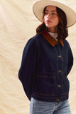 Person wearing a denim jacket with a brown collar against a beige background