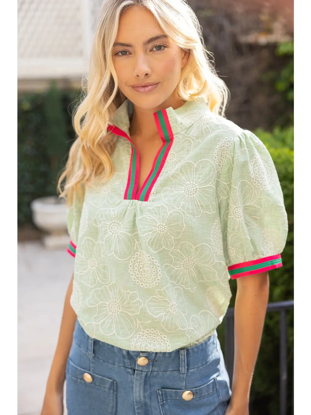 Woman wearing a light green blouse with red and green trim outdoors
