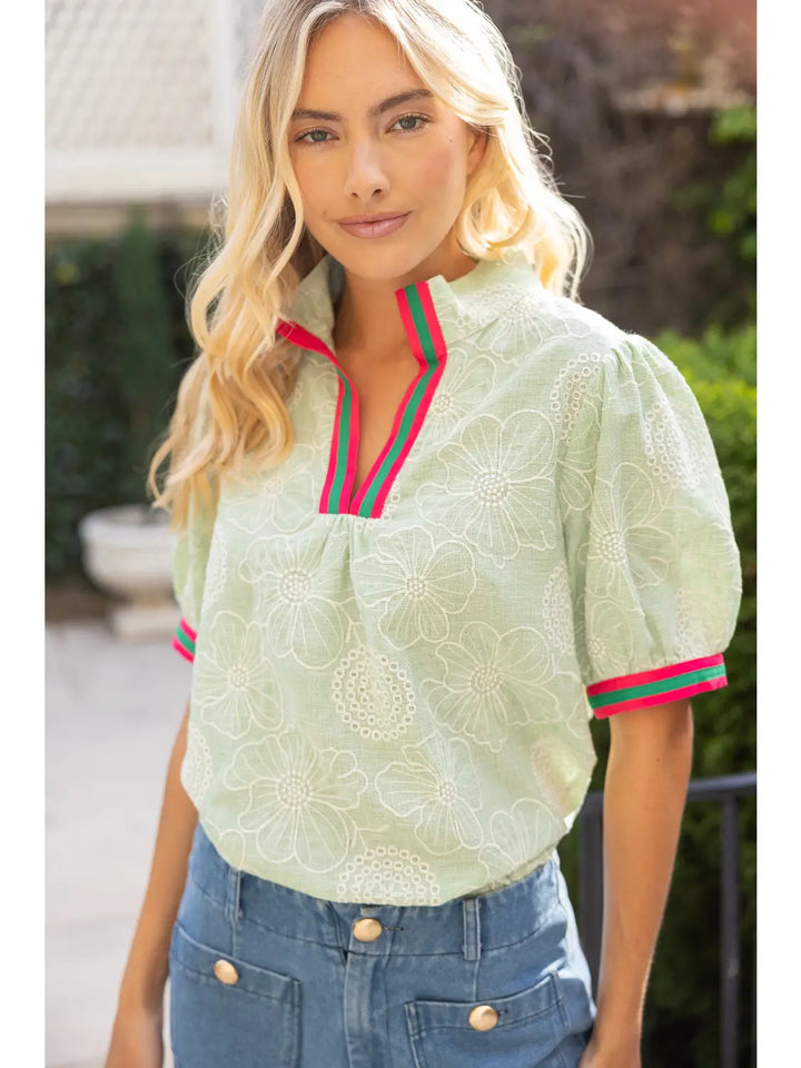 Woman wearing a light green blouse with red and green trim outdoors