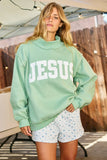 Person wearing a light green 'JESUS' sweatshirt and floral shorts outdoors.