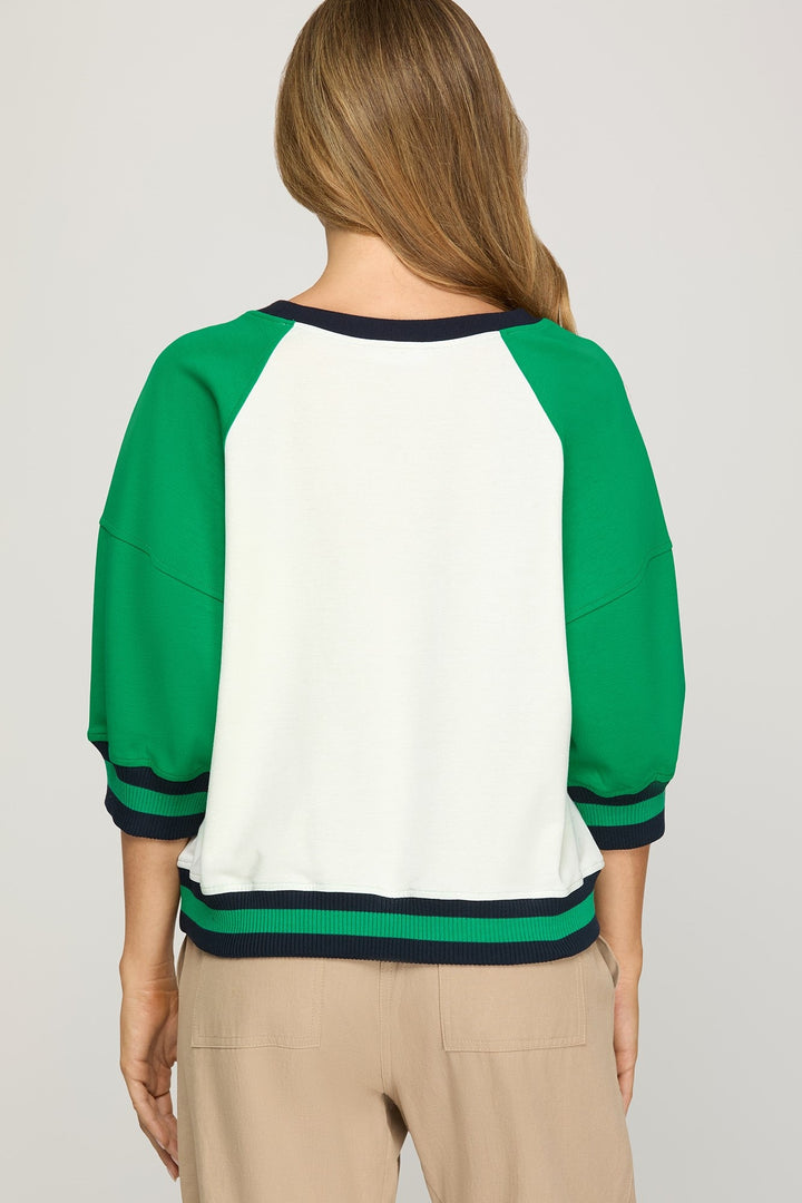 Green and white baseball-style shirt worn by a person on a plain background