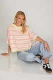 Woman wearing a striped sweater and jeans sitting on a white surface.