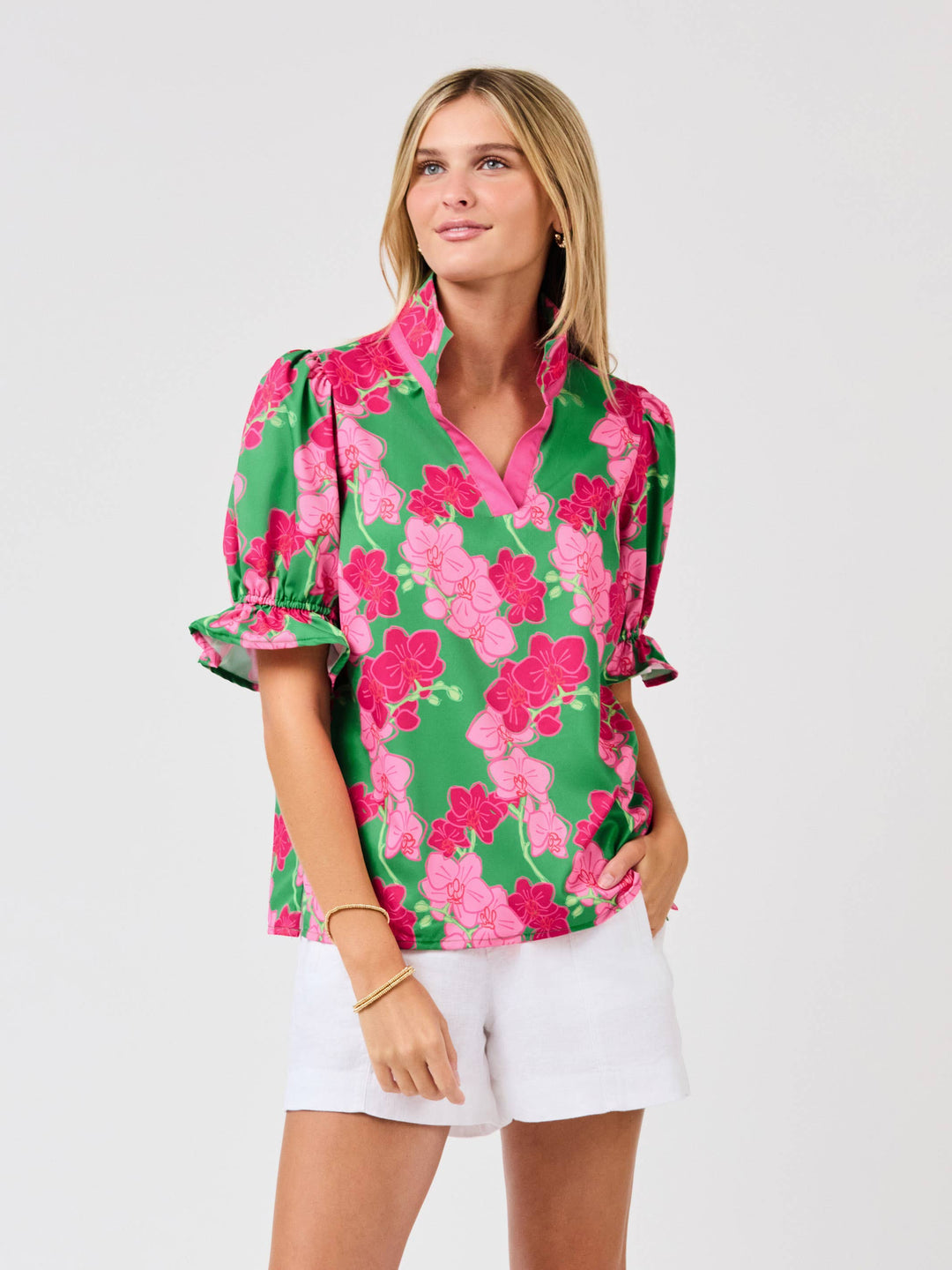 Woman wearing a floral blouse with green, pink, and white pattern on a plain background