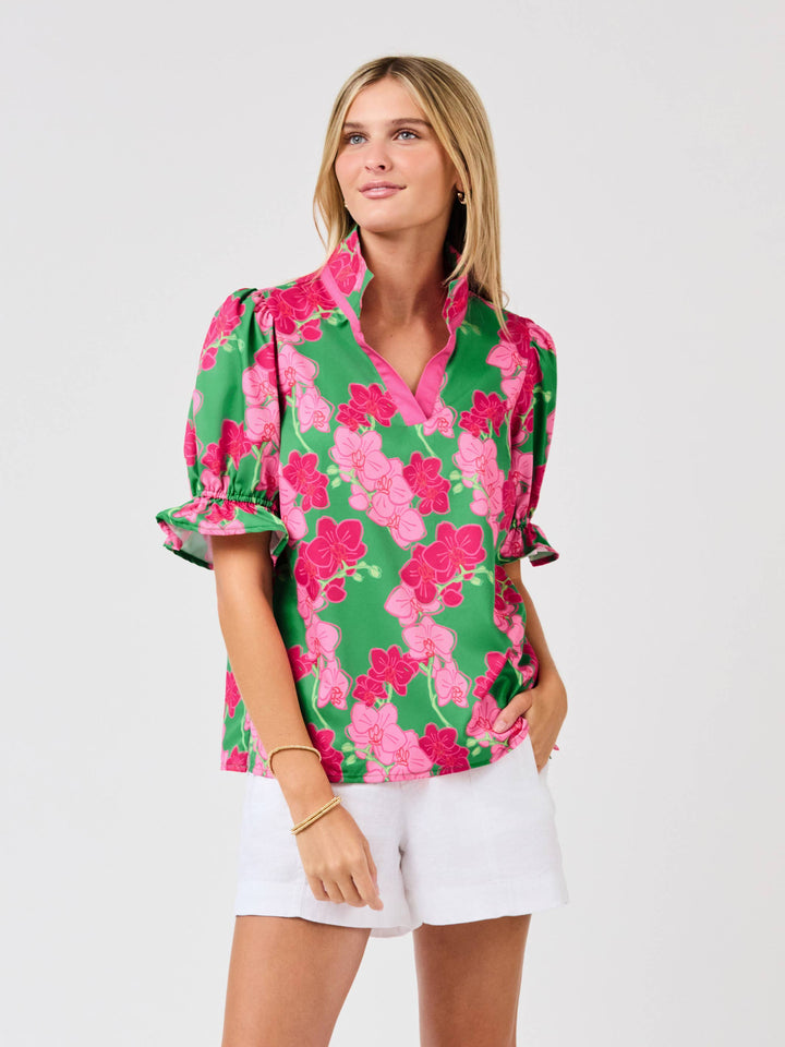 Woman wearing a floral blouse with green, pink, and white pattern on a plain background
