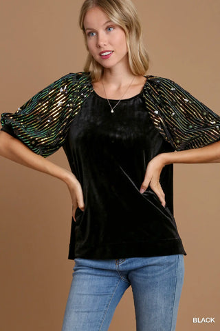 Woman wearing a black top with gold accents and blue jeans on a brown background