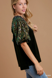 Woman wearing a black top with a green sequin detail on a beige background