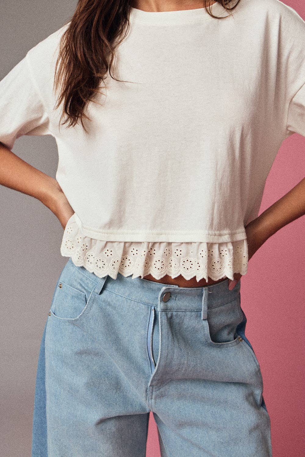 Person wearing a white blouse with lace trim and light blue jeans against a pink and gray background