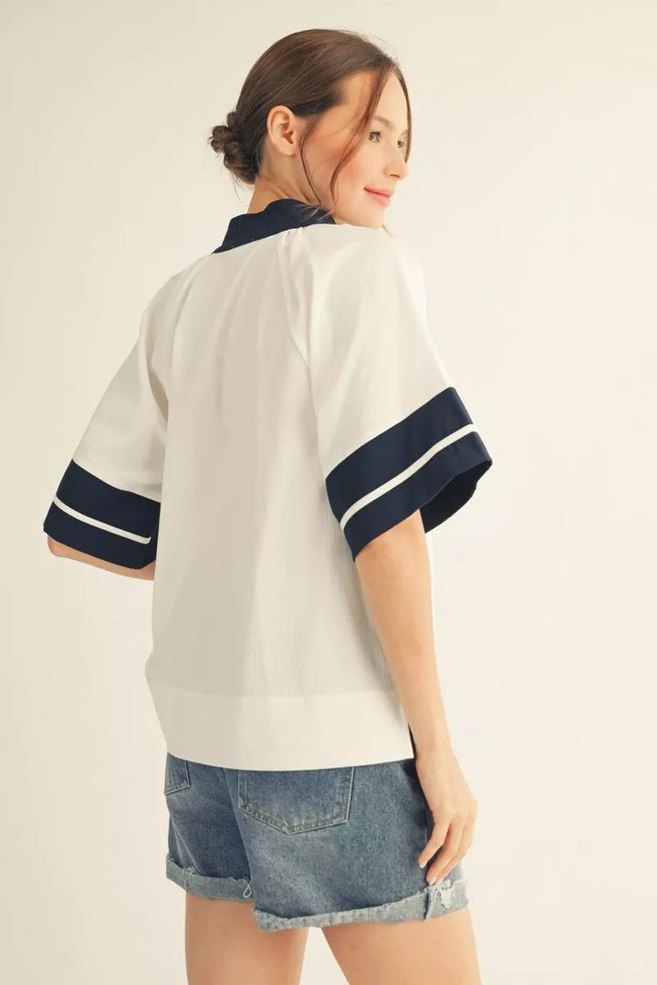 Woman wearing a white shirt with navy accents and denim shorts on a plain background